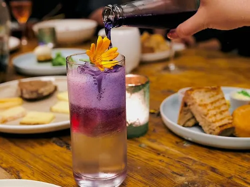 Purple drink poured into glass with flower garnish.