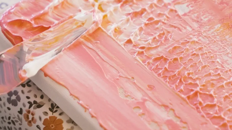 Spachtel verteilt rosa Farbe auf Leinwand.