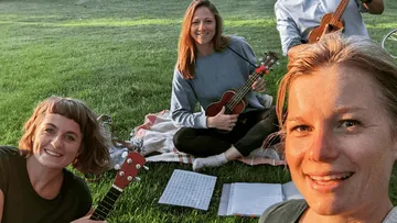 People playing ukuleles on grass, smiling.