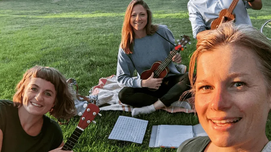 People playing ukuleles on grass, smiling.