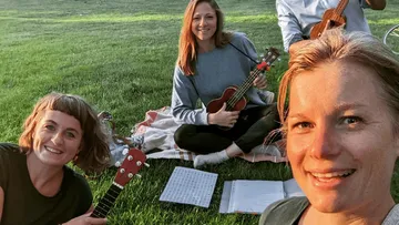 Four people playing ukuleles on grass.