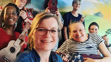 Group of smiling people holding ukuleles indoors.
