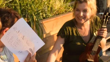 Woman with ukulele smiling outdoors.