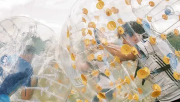 Leute spielen Bubble Soccer im Freien auf Rasen.