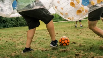 People playing bubble soccer on grass field.