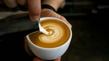 Person pouring latte art into coffee mug.