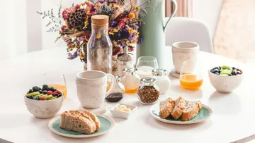 Breakfast table with bread, fruits, drinks, flowers.