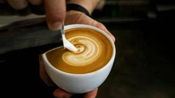 Barista gießt Latte-Art in Kaffeetasse.