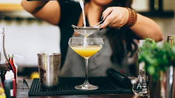 Bartender straining cocktail into glass at bar.