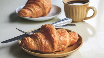 Croissant auf Teller mit Kaffee und Besteck.