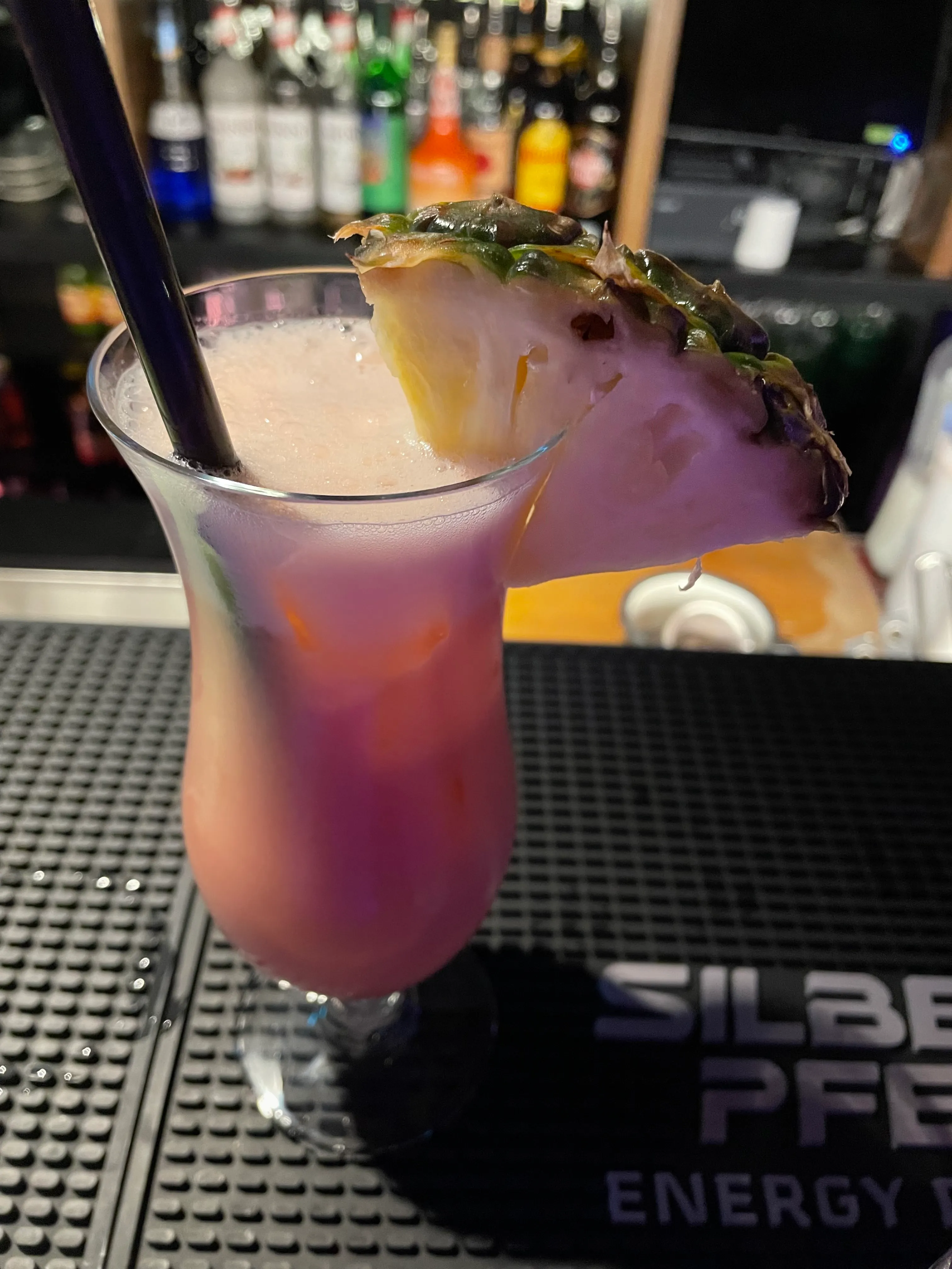Pink cocktail with pineapple garnish at bar.