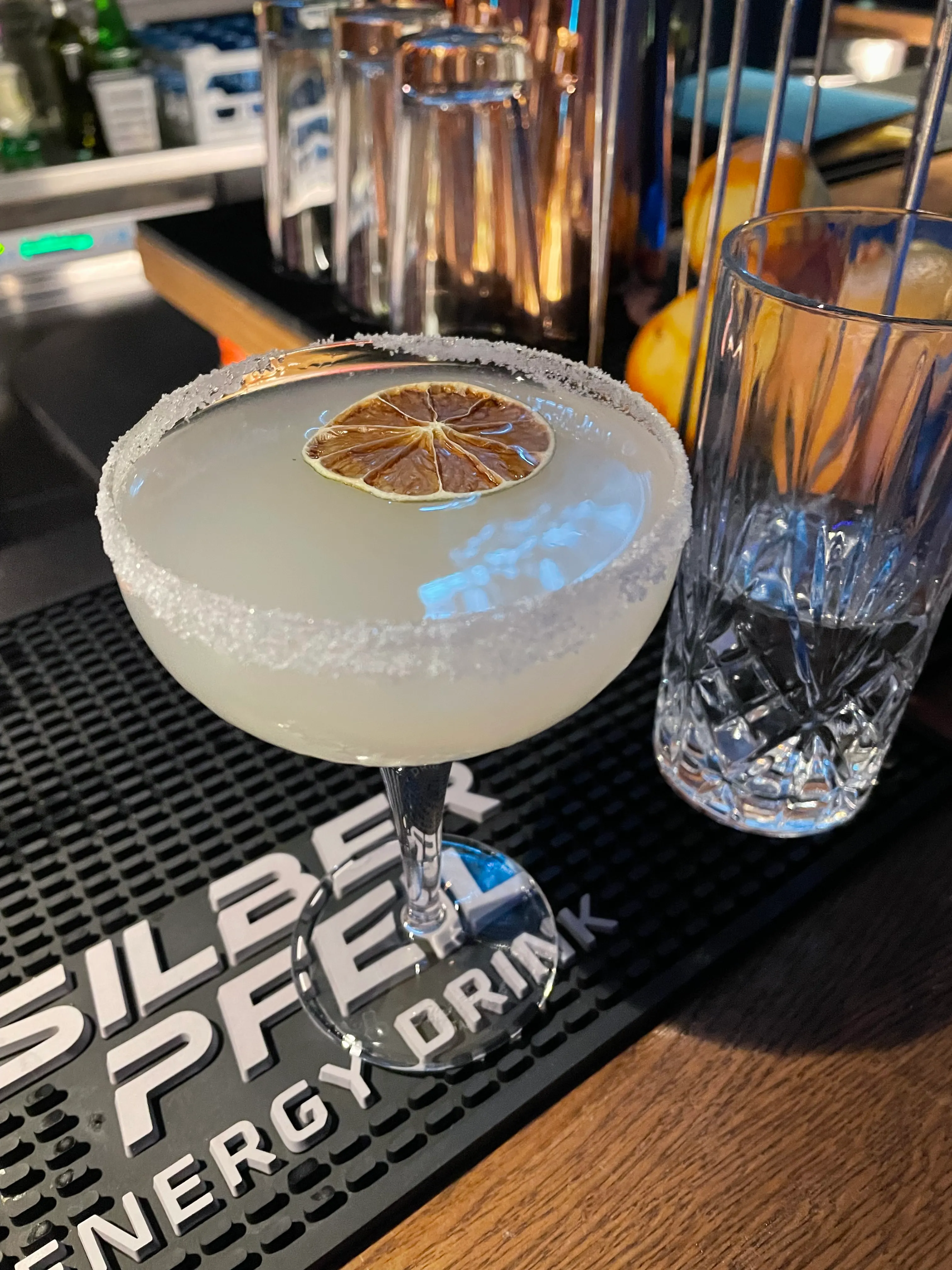 Cocktail with dried lime on bar mat.