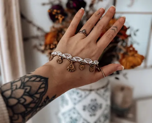 Hand trägt Armband, Tattoos sichtbar, unscharfer Hintergrund.