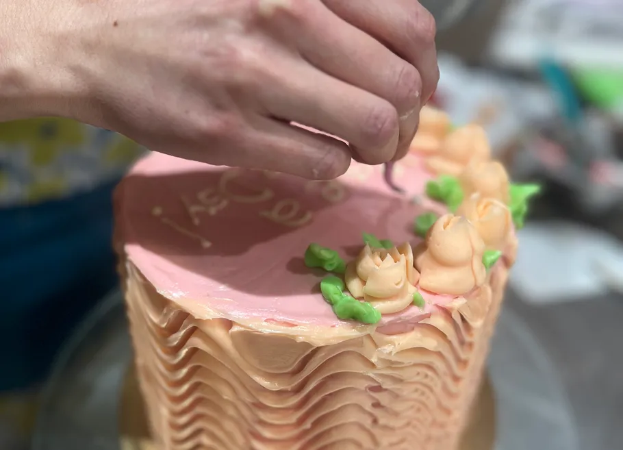 Hand decorating cake with frosting flowers.