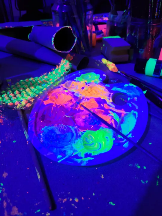 Paint palette glowing under blacklight, dark room.