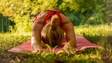 Woman practicing yoga on a mat outdoors.