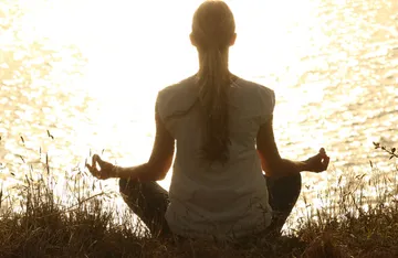 Person meditating by sunny water.