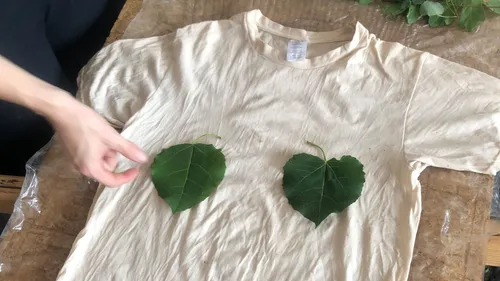Hand placing leaves on a white t-shirt.