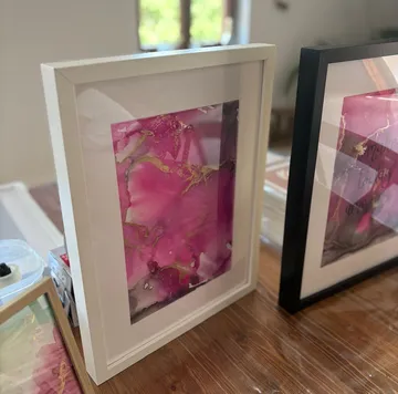 Gerahmte abstrakte Kunst mit Rosa auf Tisch.