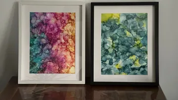 Two framed abstract paintings on wooden table.