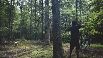 Person practicing archery in a forest.
