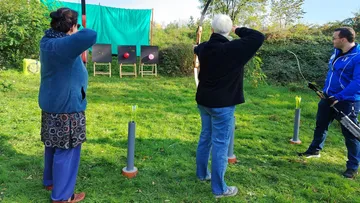 Personen üben Bogenschießen auf einer Wiese.