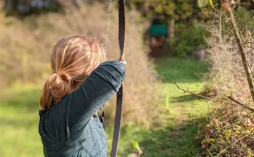 Person zielt mit Bogen in bewaldetem Gebiet.