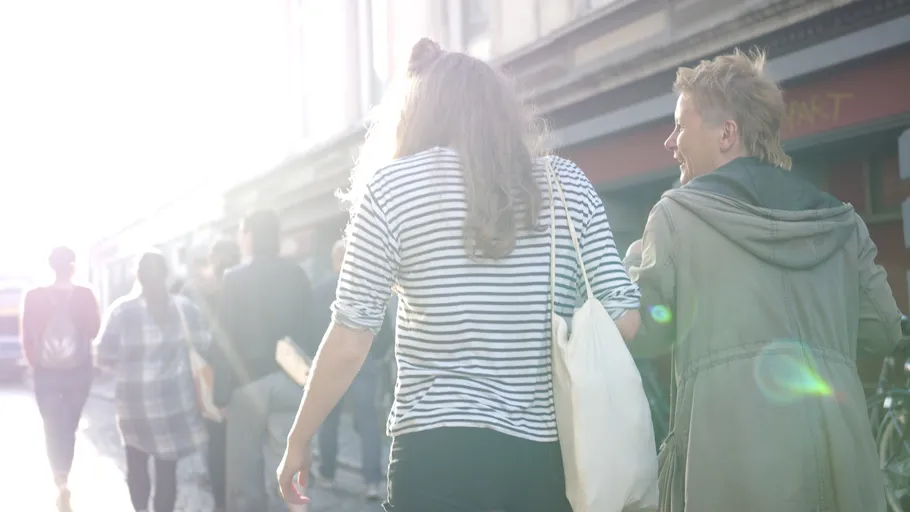 Two people walking on sunlit street.