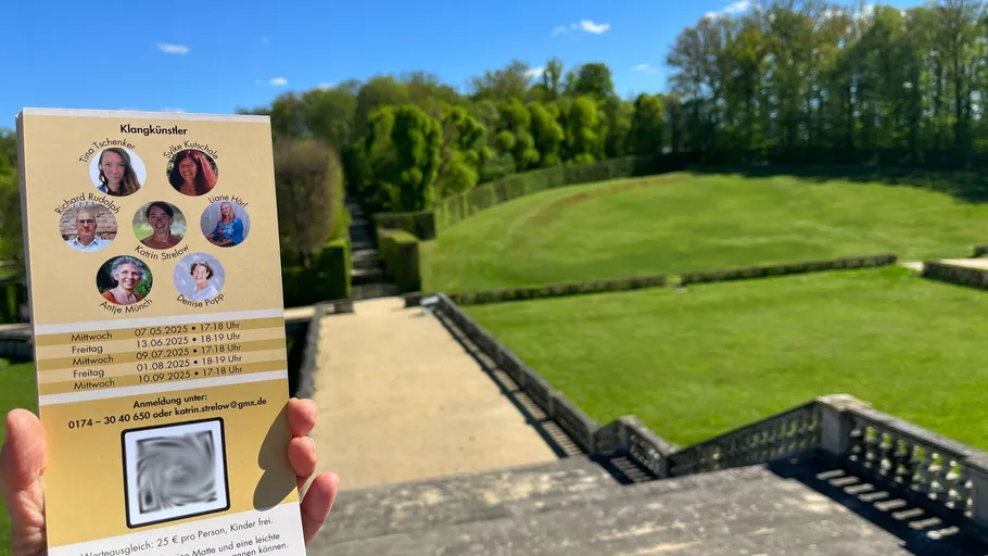 Hand hält Flyer, Garten im Hintergrund.