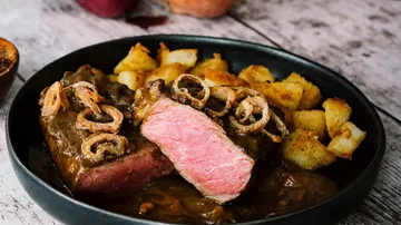 Steak with sauce and potatoes on plate.