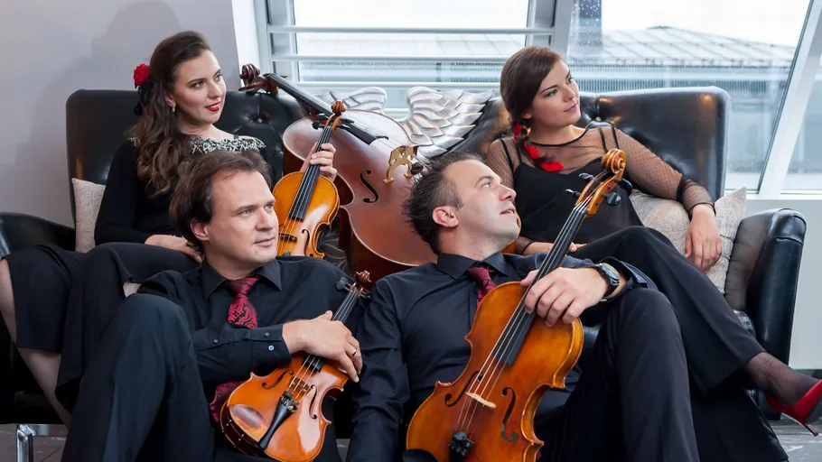 Four musicians with string instruments sitting indoors.