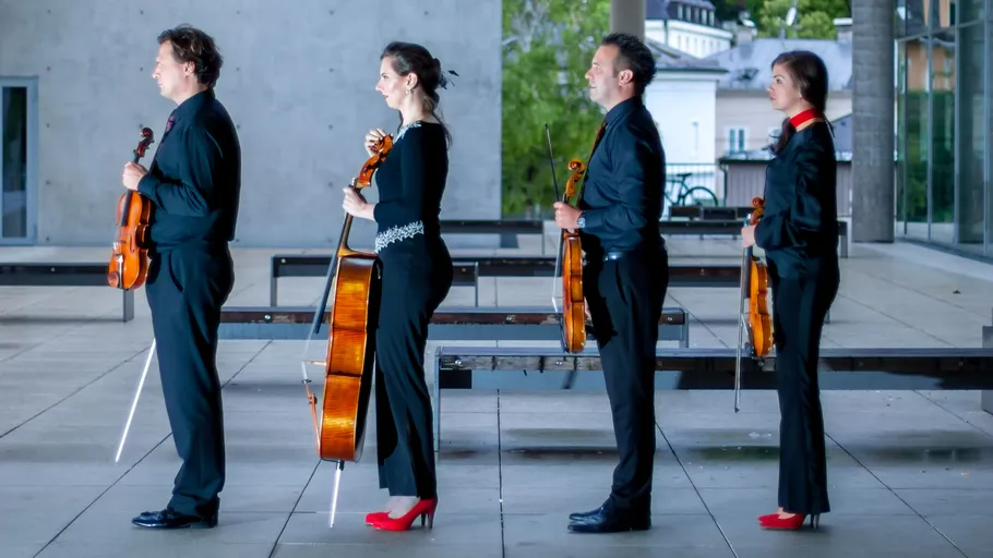 Four musicians with instruments standing indoors.