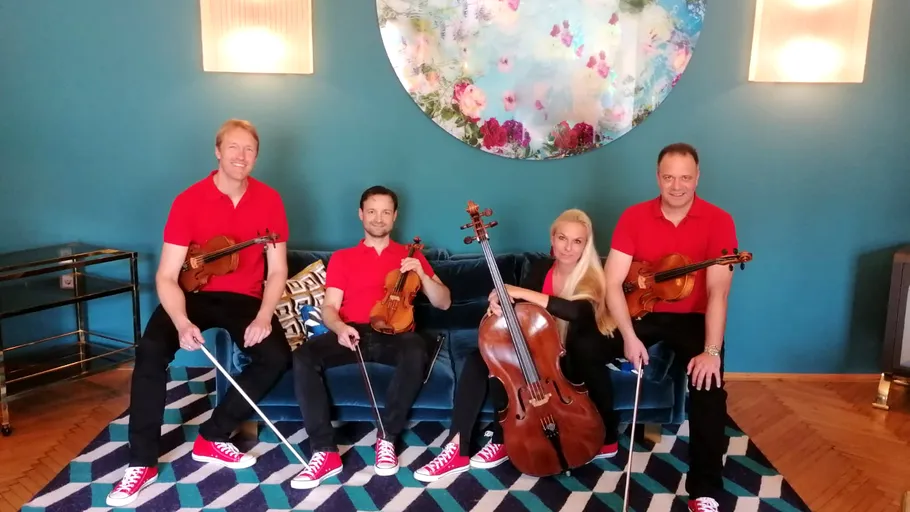 Four musicians seated indoors with instruments.