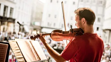 Violinist playing on outdoor stage, audience watching.