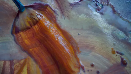 Paintbrush sweeping orange paint on surface.