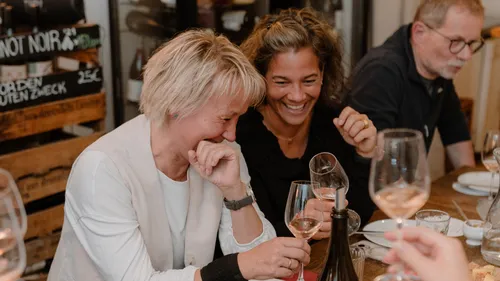 Three people laughing, holding wine glasses, indoors.