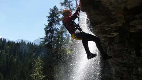 Person abseiling near waterfall in forest.