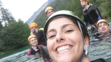 Group of people smiling in river with helmets.