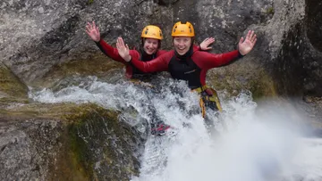 Zwei Personen in Neoprenanzügen rutschen Felsen hinunter.