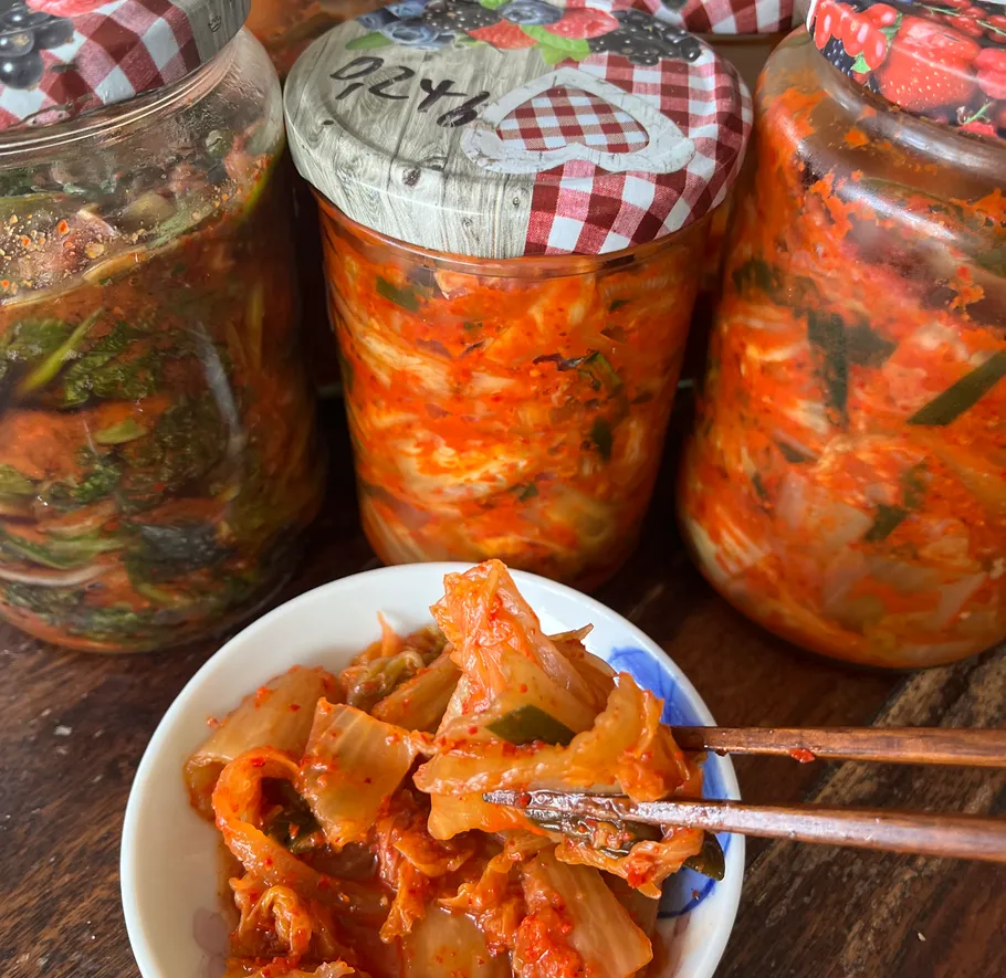 Kimchi in Gläsern und Schale mit Stäbchen.