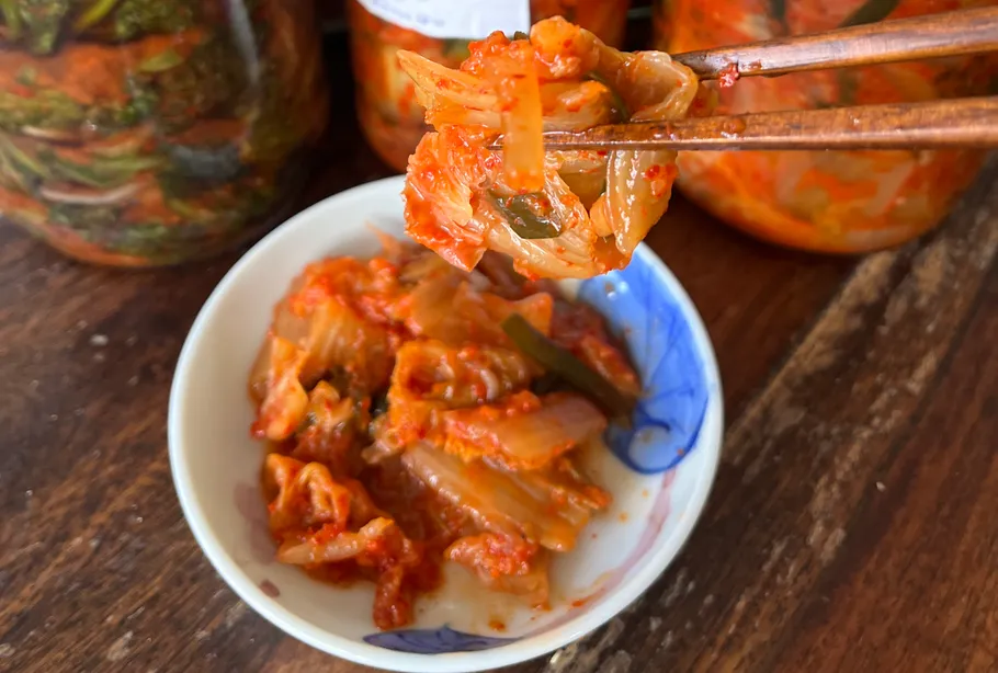 Kimchi held with chopsticks above bowl.