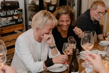 Menschen lachen und trinken an einem Tisch.