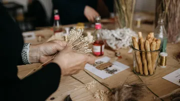 Hands arranging dried flowers on wooden table.