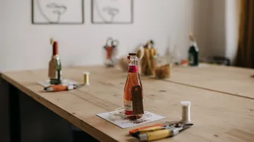 Bottle with label on wooden table, tools nearby.