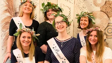 Six women with flower crowns smile indoors.