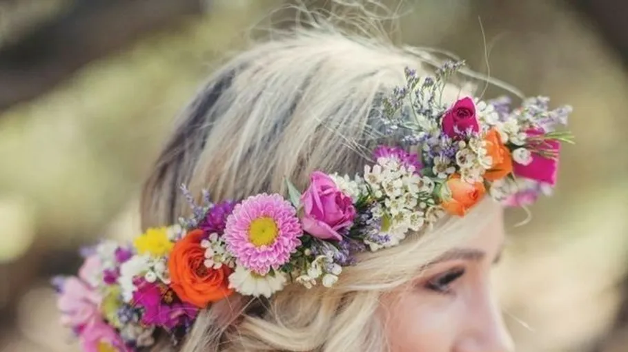 Floral crown adorns woman's blonde hair outdoors.