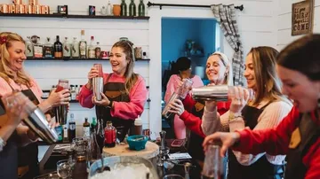 Group of women shaking cocktail shakers, smiling indoors.