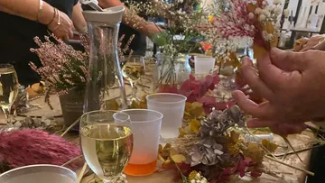 Leute arrangieren Blumen mit Getränken auf Tisch.