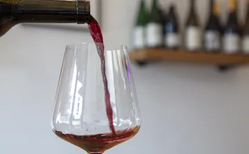 Rotwein wird in Glas gegossen, Flaschen im Hintergrund.