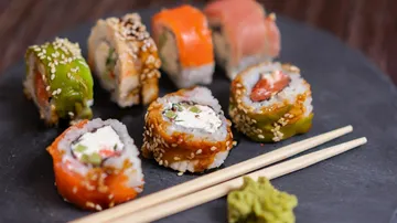Sushirollen auf Schieferplatte mit Stäbchen.